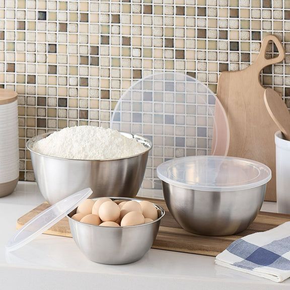 Metal mixing bowls with flour, eggs, and a tiled backsplash in a kitchen setting.