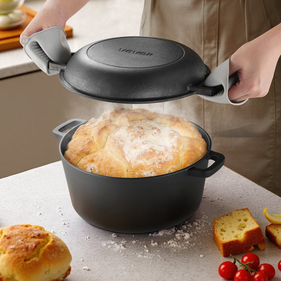 Person lifting the lid of a black cast iron pot containing bread, with a kitchen setting in the background.