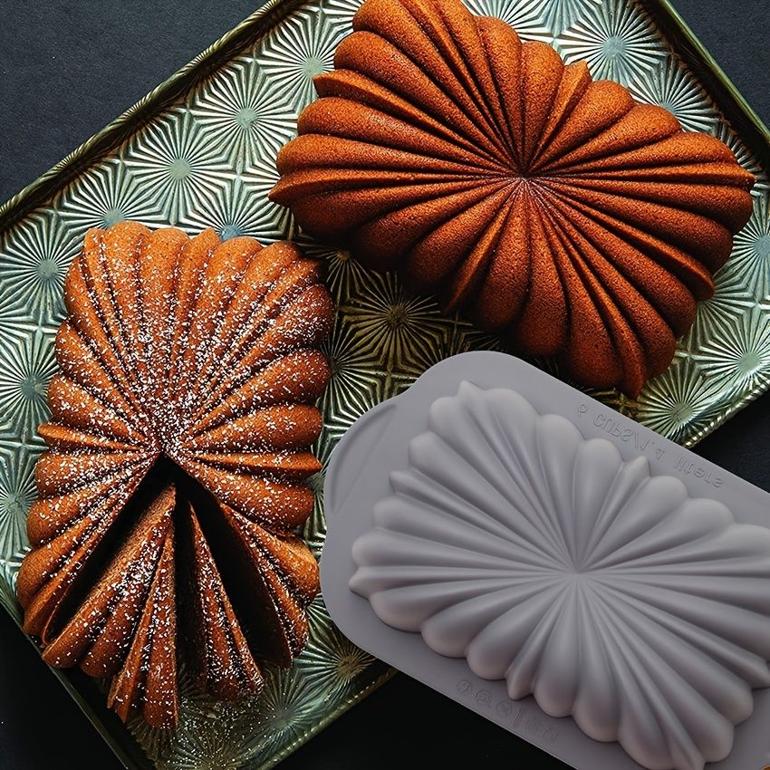 Two baked goods with a decorative pattern next to a silicone mold on a decorative tray.