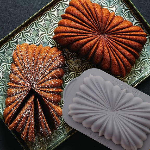 Two baked goods with a decorative pattern next to a silicone mold on a decorative tray.