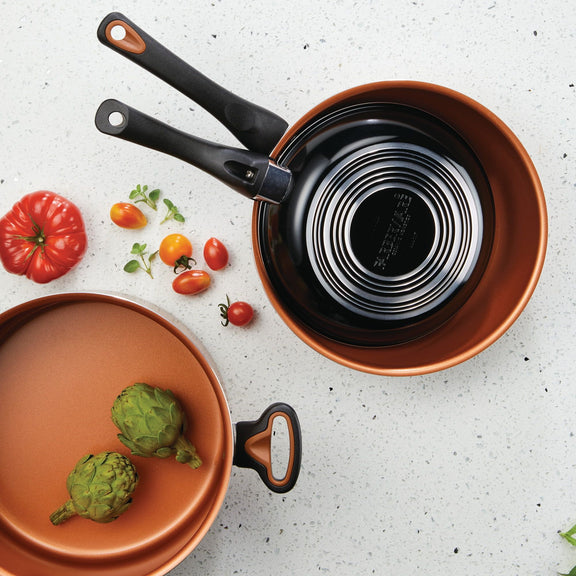 Copper cookware set with tomatoes and artichokes on a light gray surface