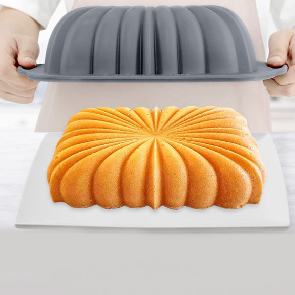Bundt cake being removed from a gray silicone bundt pan on a white surface.