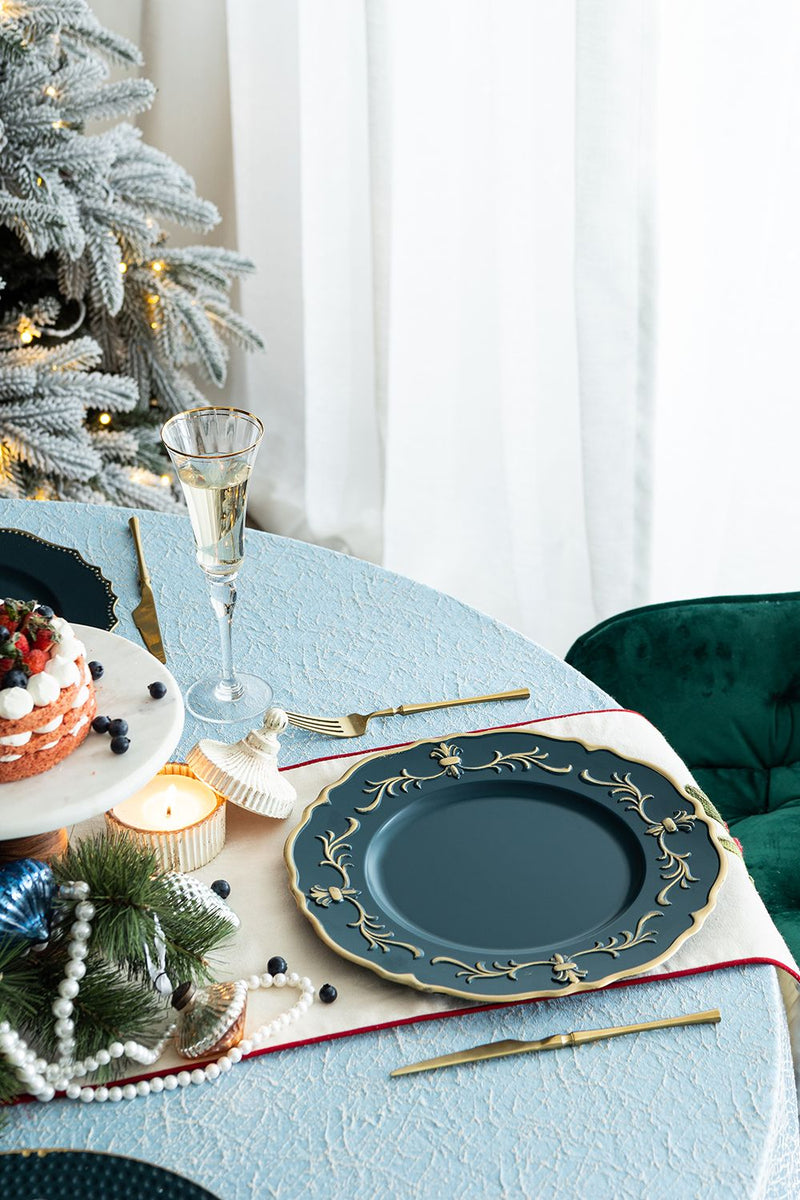 Decorative table setting with blue plates, gold cutlery, and a Christmas tree in the background.