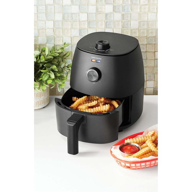 Black air fryer with fries on a white countertop with a tiled backsplash.