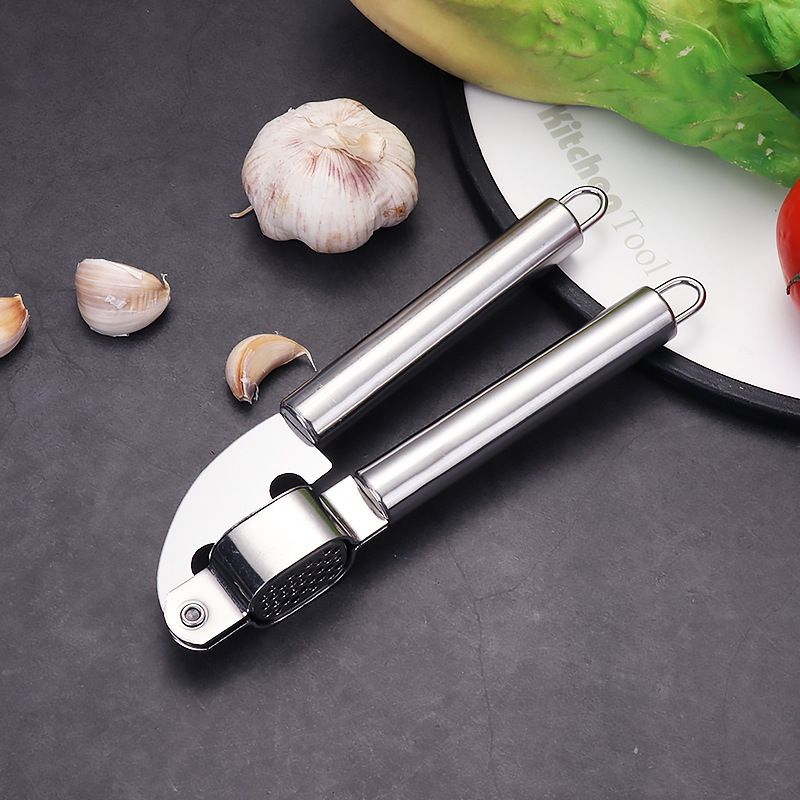 Garlic press on a dark surface with garlic cloves and a knife in the background