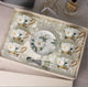 Ceramic tea set with floral design in a box on a table.