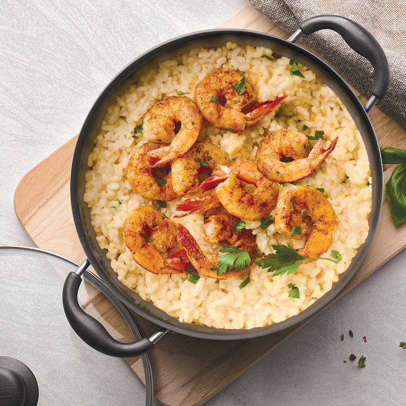 Black skillet with shrimp and risotto on a wooden board