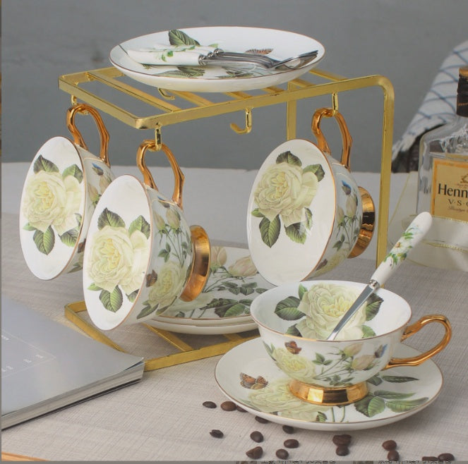 Tea set with floral design on a table with coffee beans and a laptop.