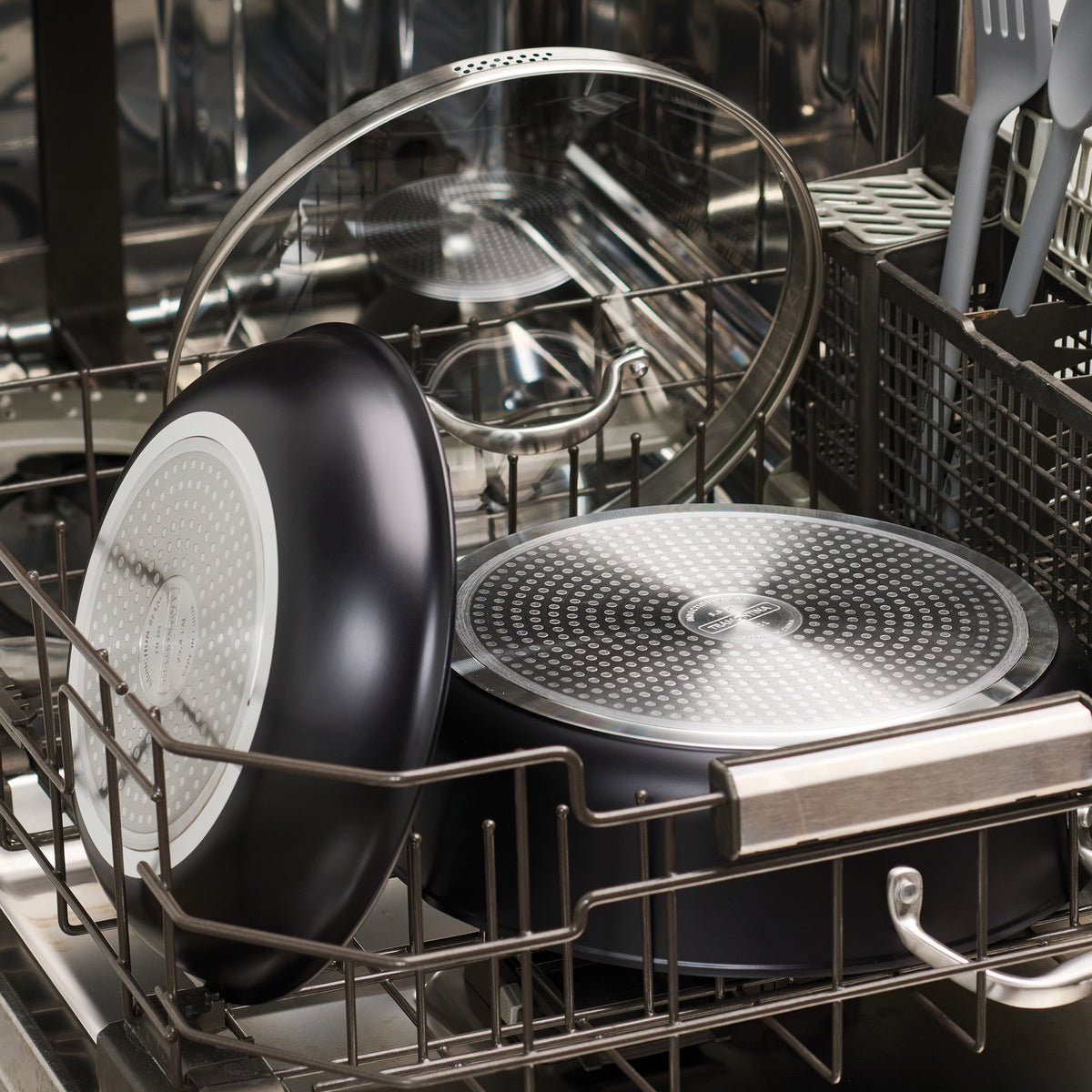 Dishwasher with dishes inside, including a black frying pan and glass bowl.