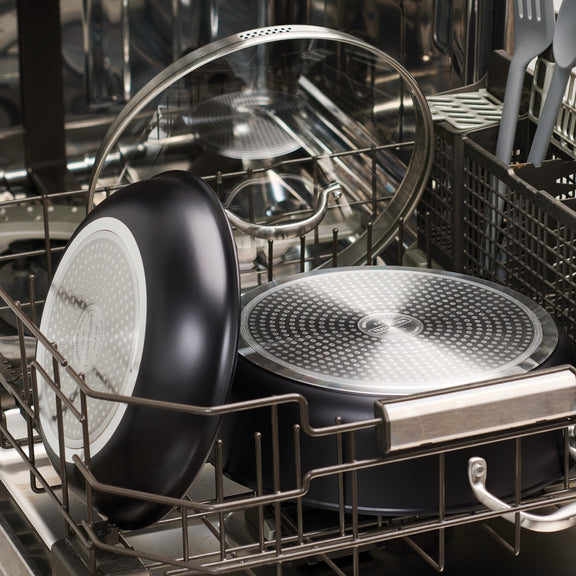 Dishwasher with dishes inside, including a black frying pan and glass bowl.