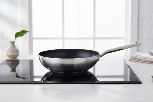 Wide stainless-steel wok-style sauté pan with dark interior on a modern induction cooktop