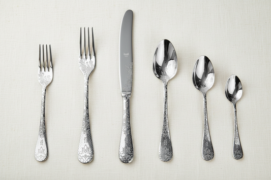 Exactly five ornate silver flatware pieces with detailed floral scrollwork on ivory linen