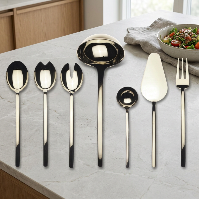 Mepra Due Champagne seven-piece serving set on a pale kitchen island beside linen and a salad bowl.