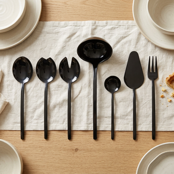 Mepra Due Oro Nero seven-piece dark serving set on ivory linen on an oak dining table.