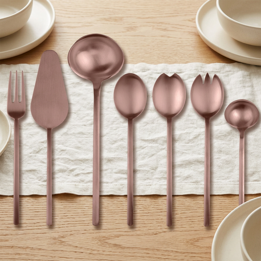 Mepra Due Ice Bronze seven-piece serving set on an oak table with ivory linen and ceramic dishes.