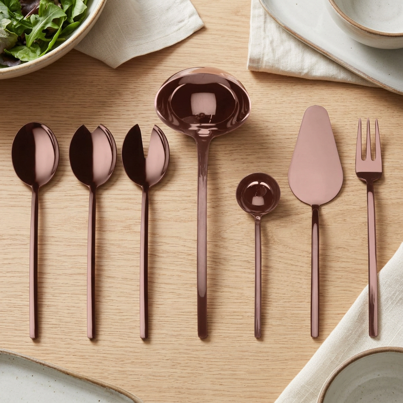 Mepra Due Bronzo seven-piece polished bronze serving set on an oak dining table with linen and ceramic dishes.