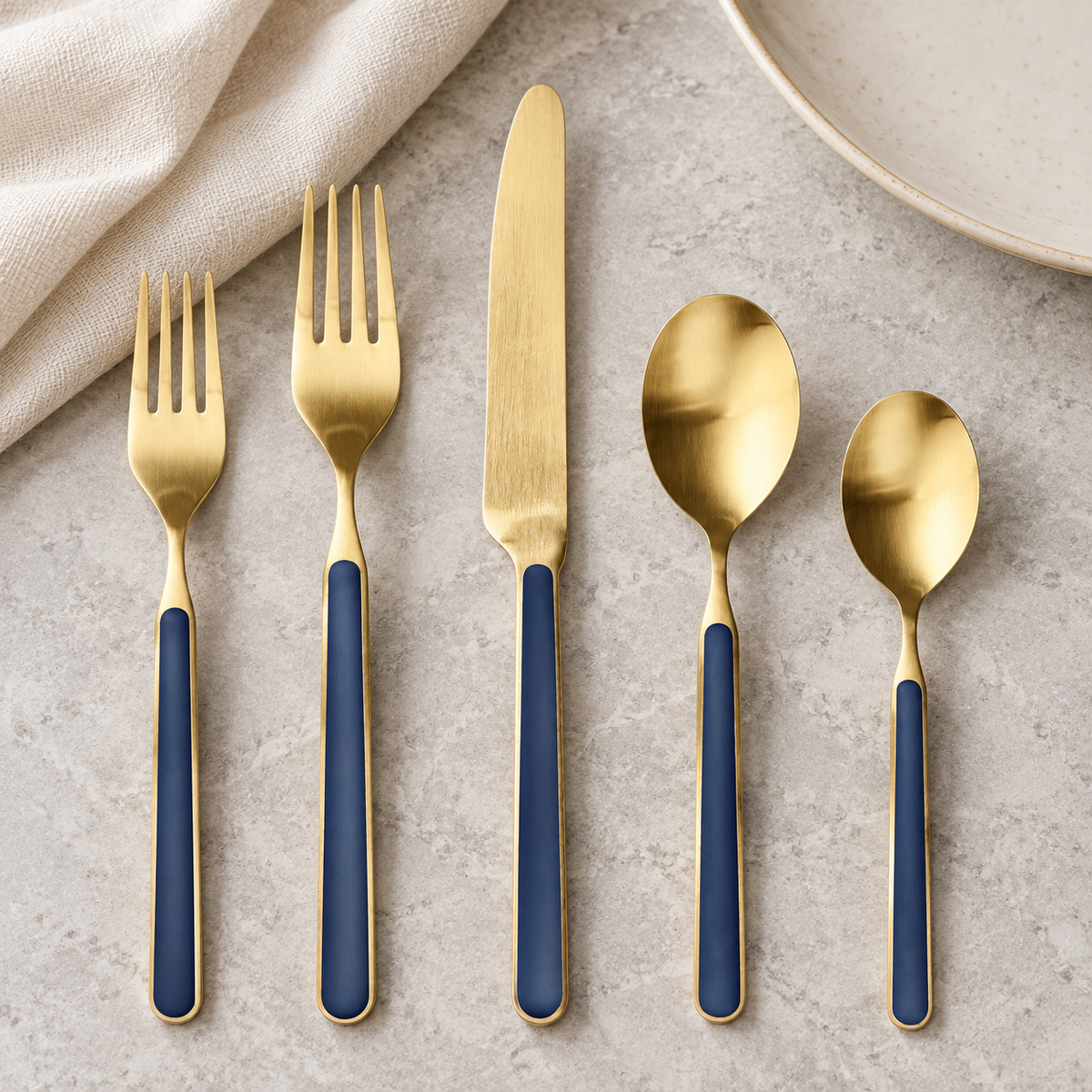 Mepra Fantasia Ice Oro Cobalt five-piece satin gold flatware on pale stone