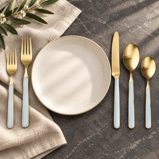 Mepra Fantasia Ice Oro Light Blue five-piece gold flatware beside an ivory plate