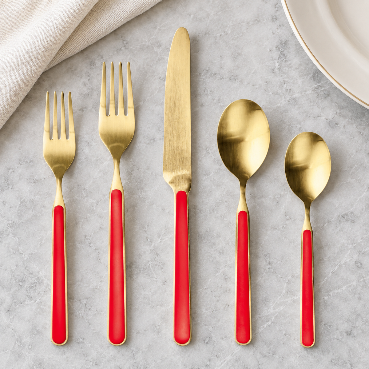 Mepra Fantasia Ice Oro Red five-piece flatware on pale stone, with brushed gold metal and red handles