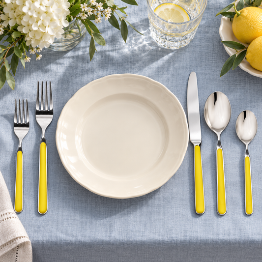 Mepra Fantasia Yellow five-piece flatware around an ivory plate on blue-gray linen