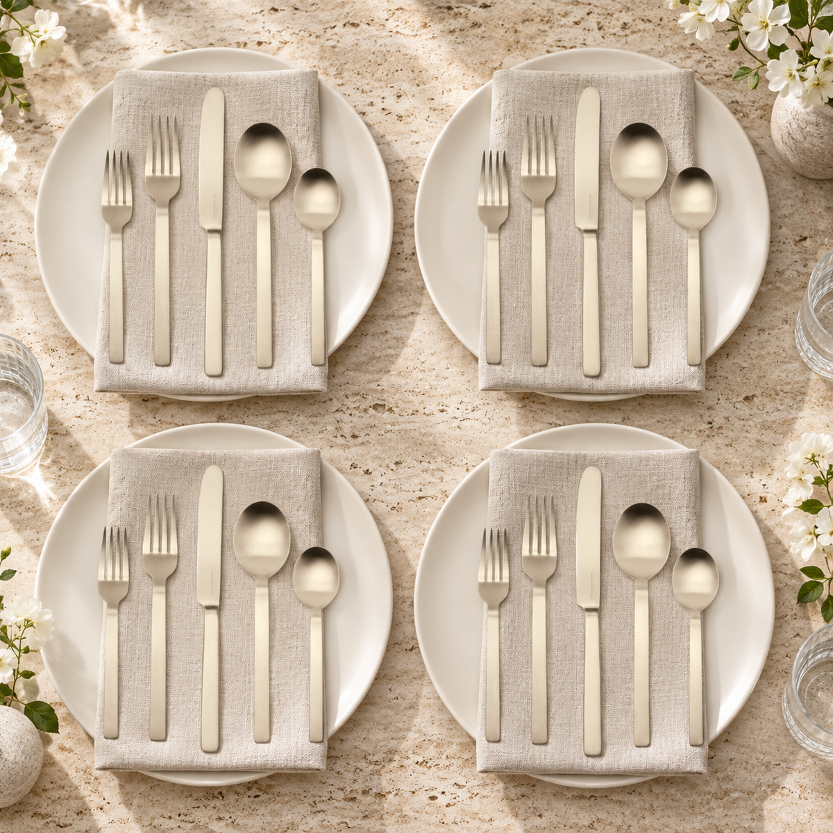 Mepra Stile Ice Champagne 20-piece flatware arranged as four luminous travertine-table place settings