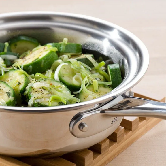 Stainless steel frying pan with zucchini and noodles on a wooden trivet