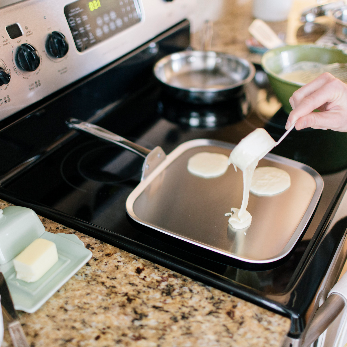 Person cooking pancakes on a griddle with a stove in the background